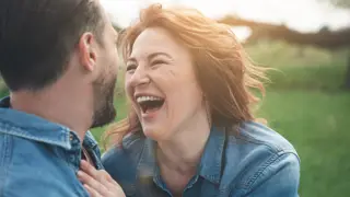 Cherishing Joyful Moments as a Carent – A middle-aged woman and man in denim jackets share a joyful moment outdoors, laughing together in a sunlit park. A theme of finding happiness and connection despite the challenges of caring for an elderly parent