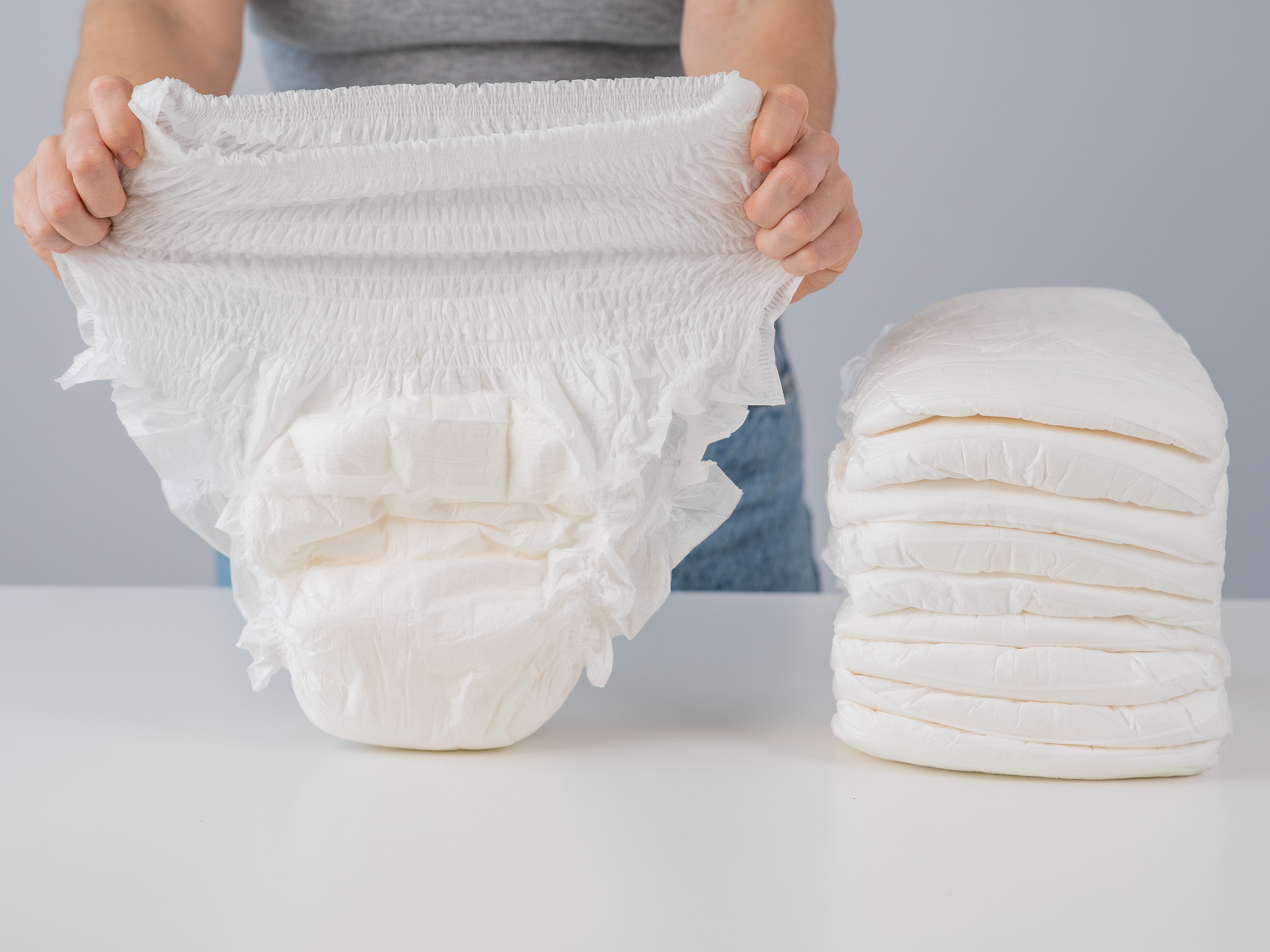 Person holding up an adult incontinence pant with a stack beside them – incontinence pants offer elderly parents discreet, comfortable protection against leaks, helping maintain dignity and hygiene throughout the day.