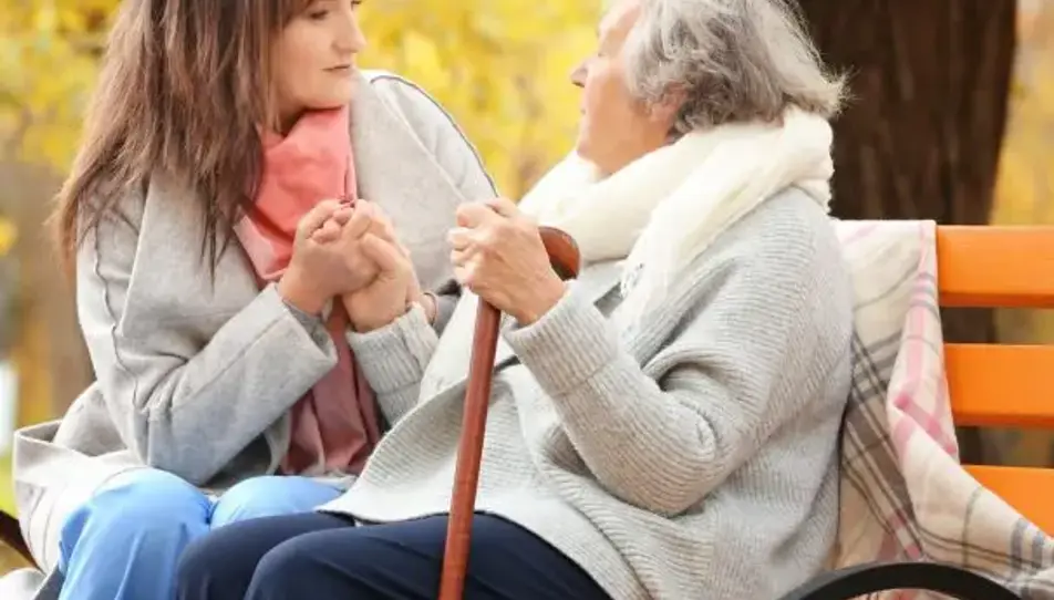 A carent and their elderly parent sitting together on a bench