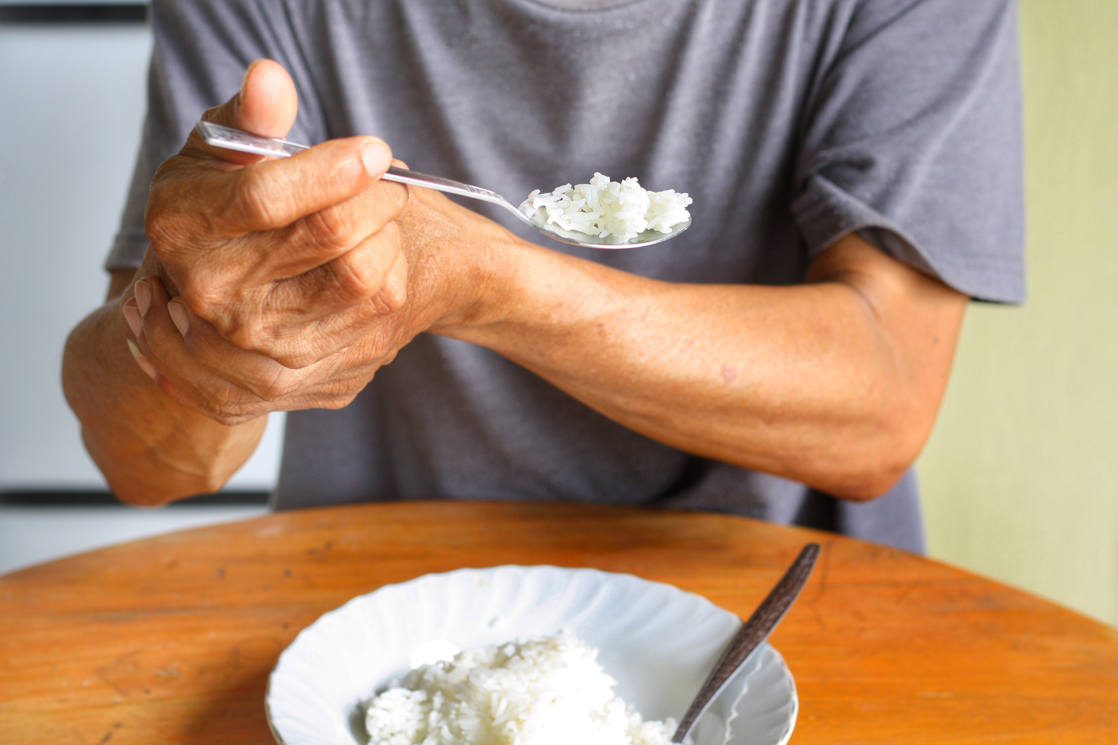Older adult eating with support from their other hand – highlighting the need for adaptive cutlery designed to help elderly parents with limited grip, arthritis, or hand tremors eat more easily and independently.
