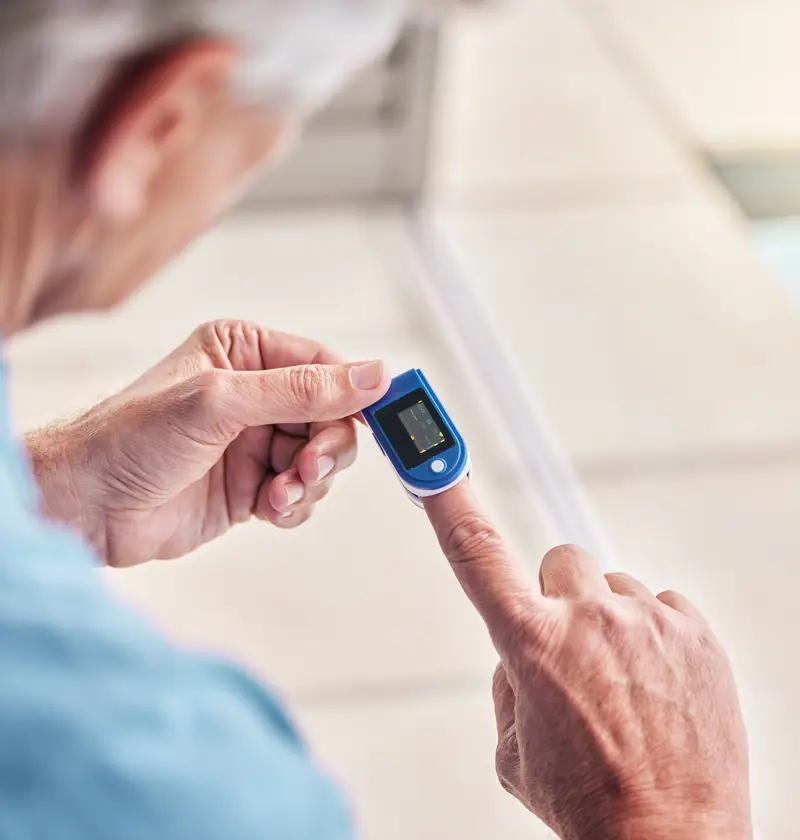Older adult using a fingertip heart rate and oxygen monitor at home – a simple, portable device ideal for carers tracking vital signs of elderly parents.