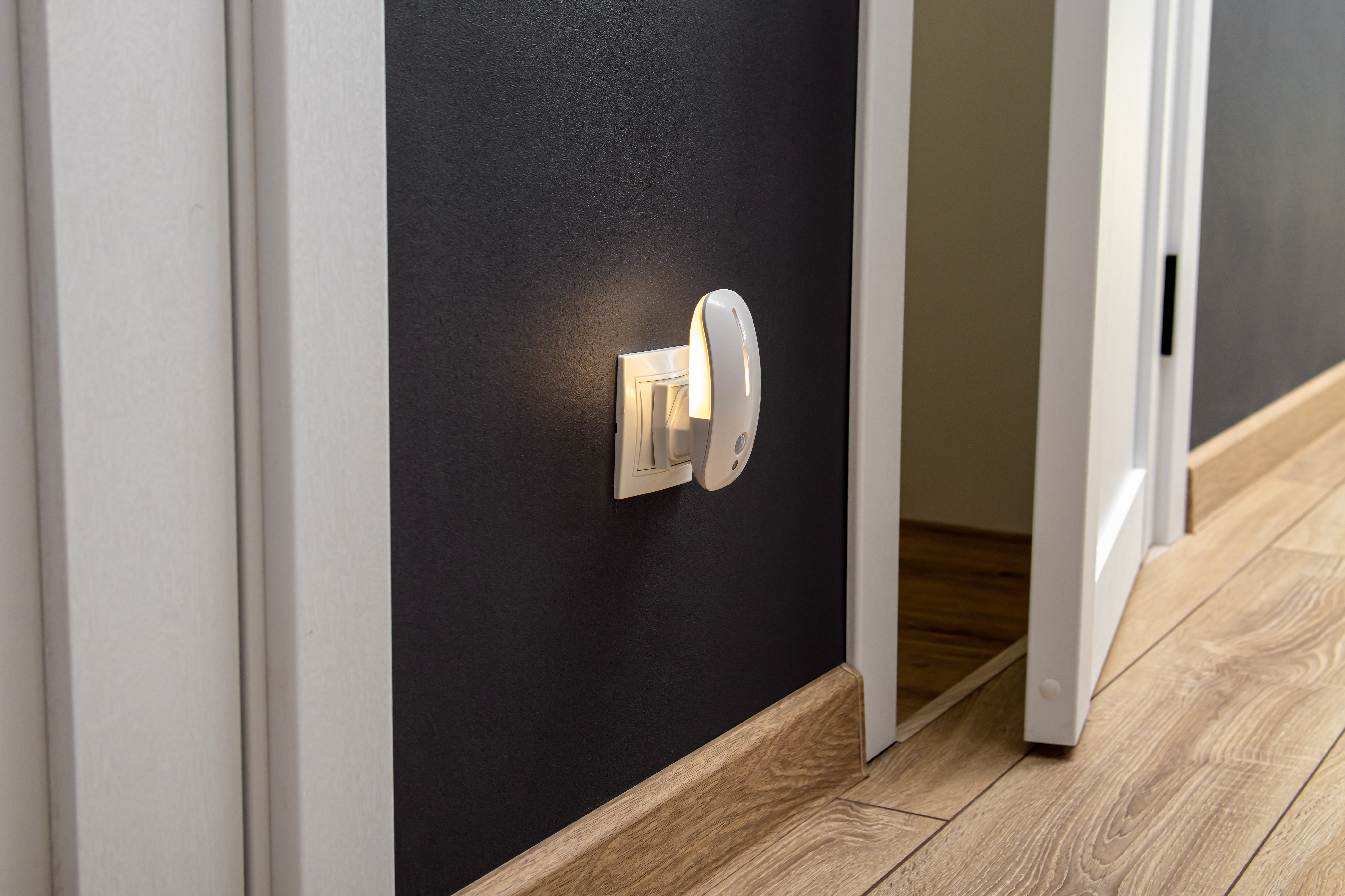 Plug-in motion sensor night light switched on in a hallway – helps elderly parents move safely around the home at night by automatically lighting dark areas without needing to search for switches.