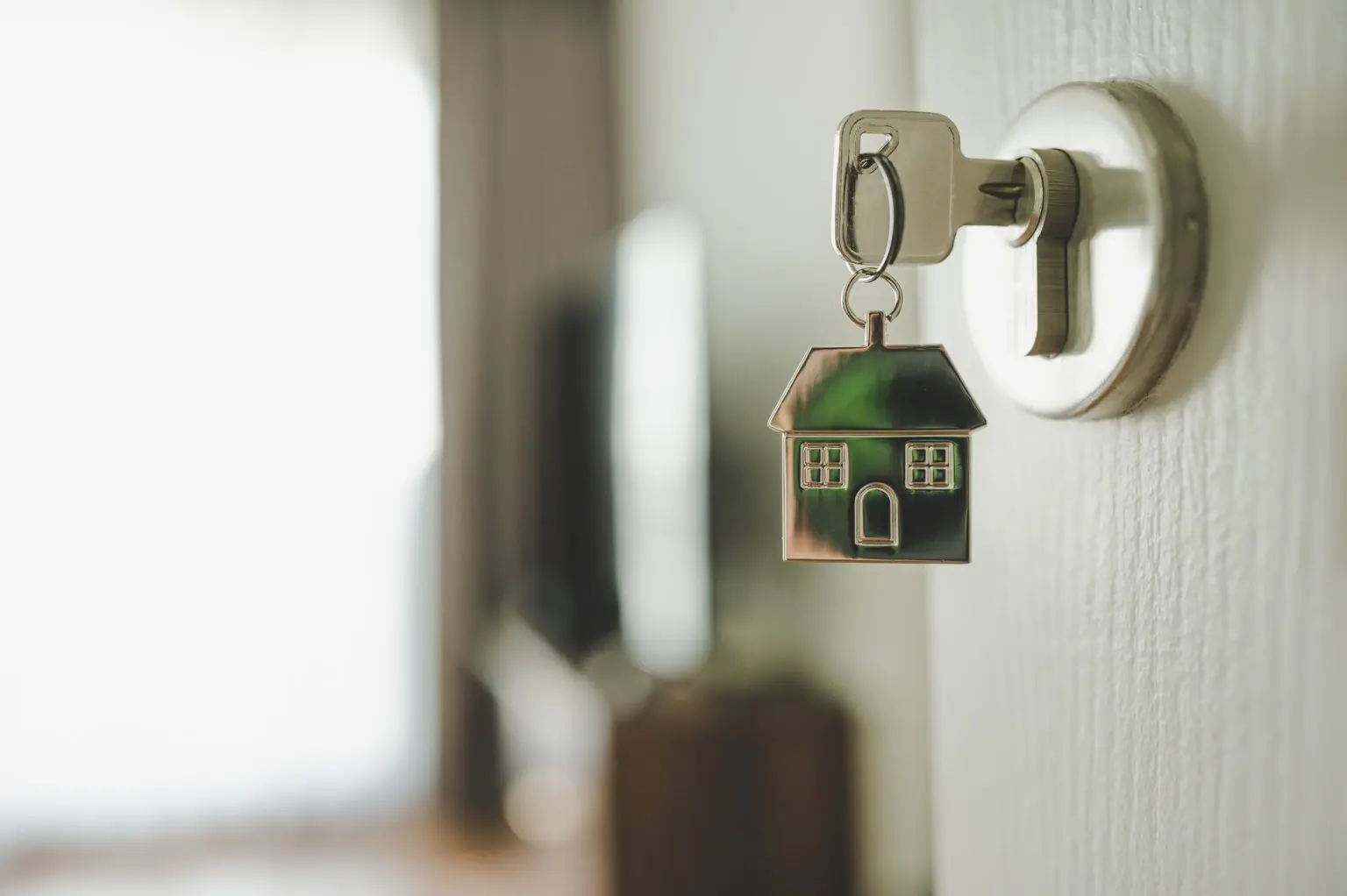 A Key in a lock into a bright home, attached is a keychain of a house