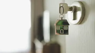 A Key in a lock into a bright home, attached is a keychain of a house