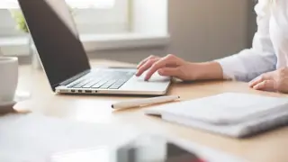 Woman sitting at a laptop with items strewn across the desk
