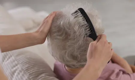 Carer gently combing an older adult’s hair – waterless hair products are a convenient option for elderly parents who have limited mobility or find regular hair washing difficult.