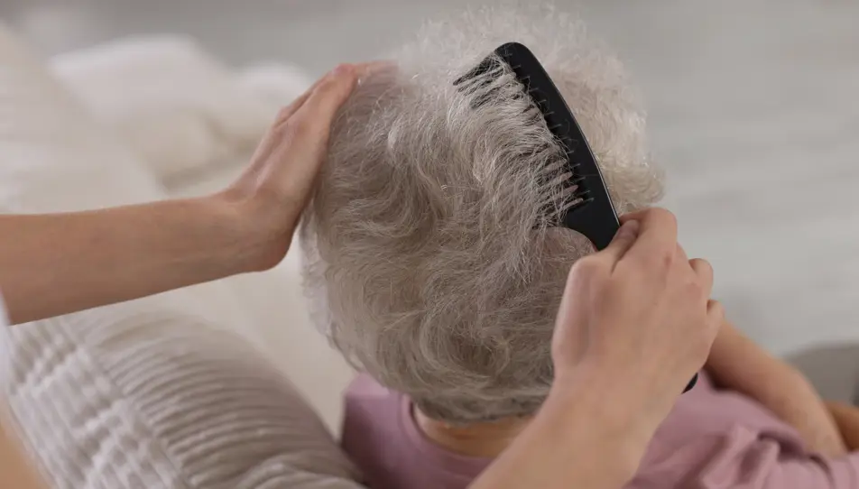 Carer gently combing an older adult’s hair – waterless hair products are a convenient option for elderly parents who have limited mobility or find regular hair washing difficult.