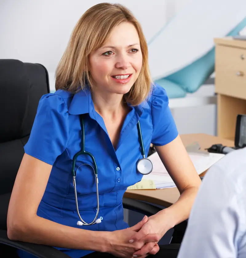 Consulting a GP About Elderly Parent’s Health – A female doctor in a blue uniform listens attentively to a patient. A reminder of the importance of regular check-ups and seeking professional medical advice for elderly loved ones.