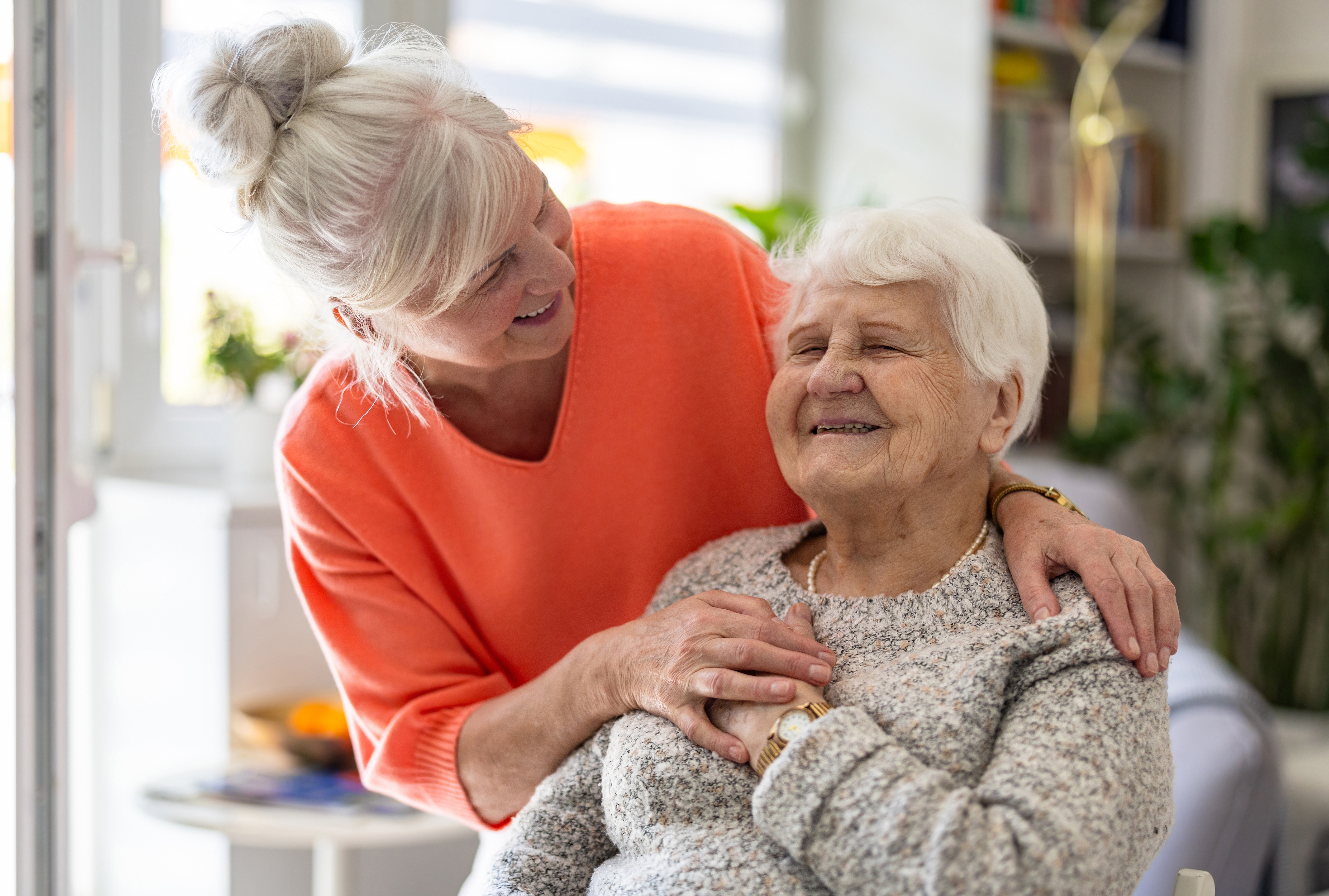Woman in orange jumper hugging older woman, both smiling
