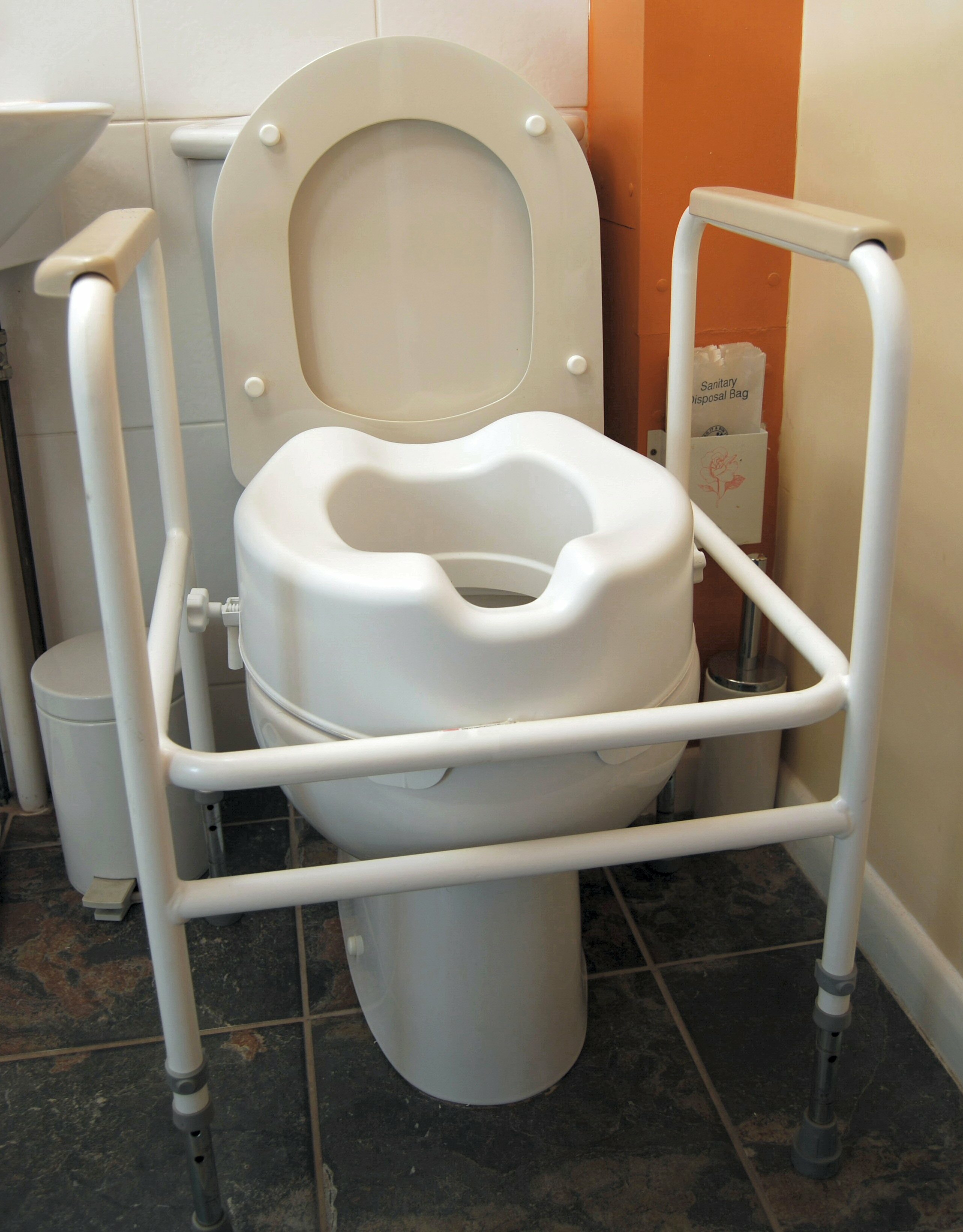 Toilet fitted with a raised seat and support frame – toilet seat risers help elderly parents with limited mobility sit and stand more easily, reducing strain and supporting safer bathroom use.