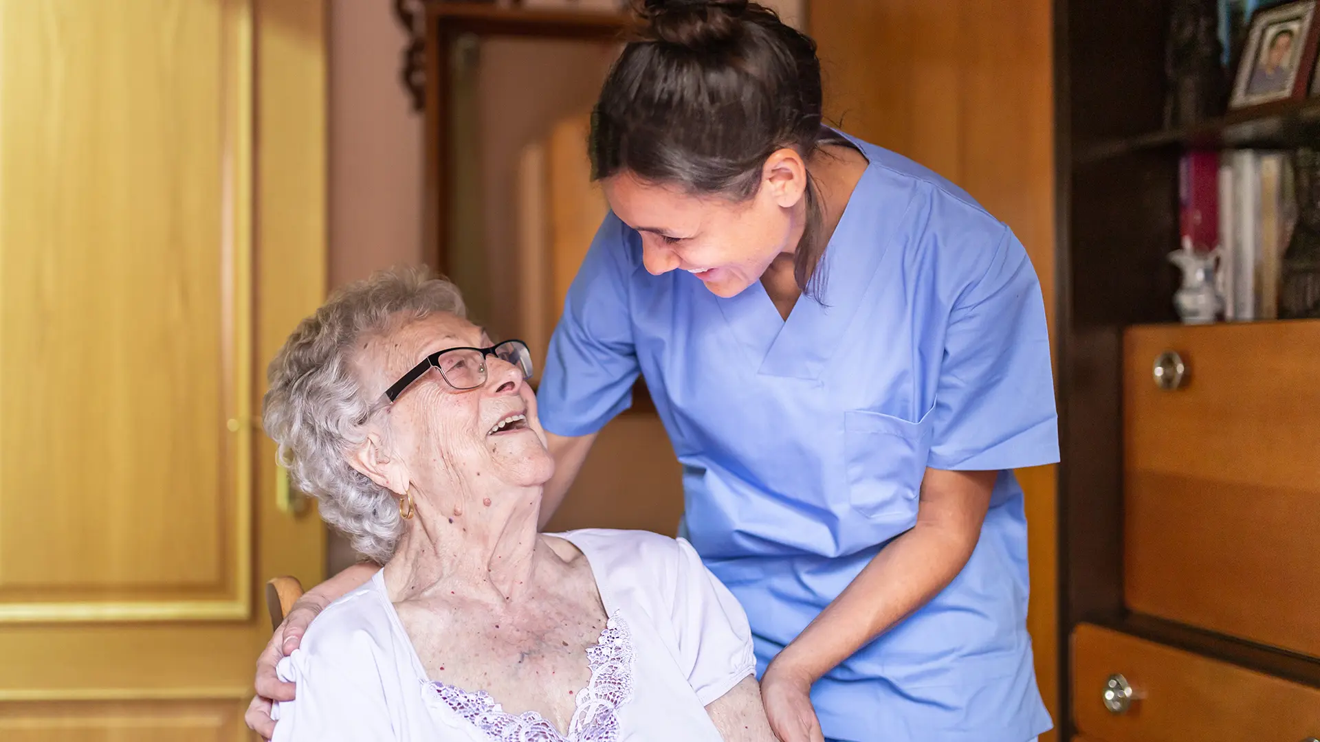Elderly parent in a care home being looked after by a young female nurse