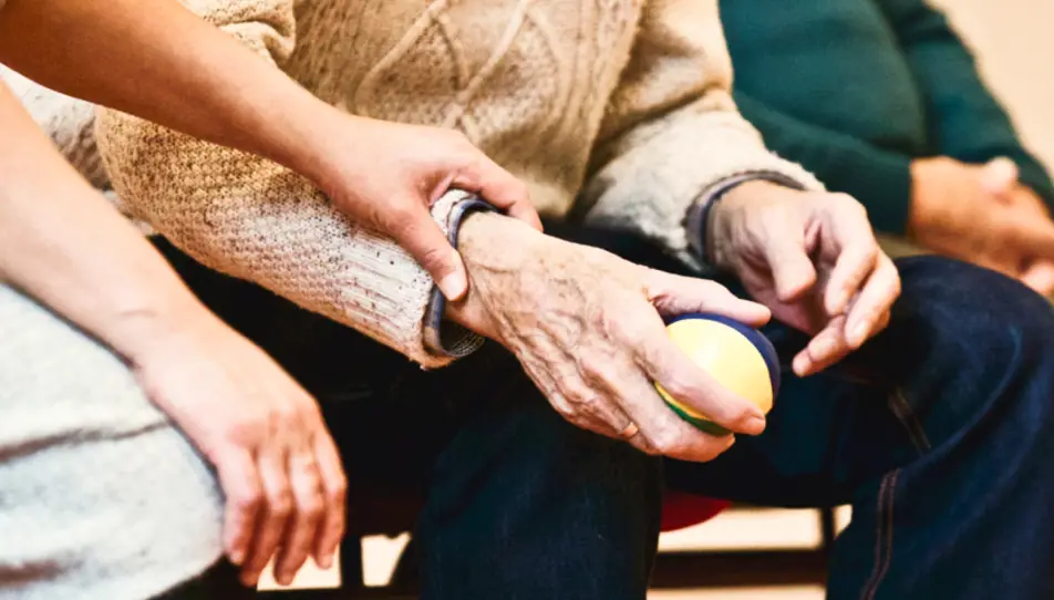 An elderly person holding a ball and being helped by a carent