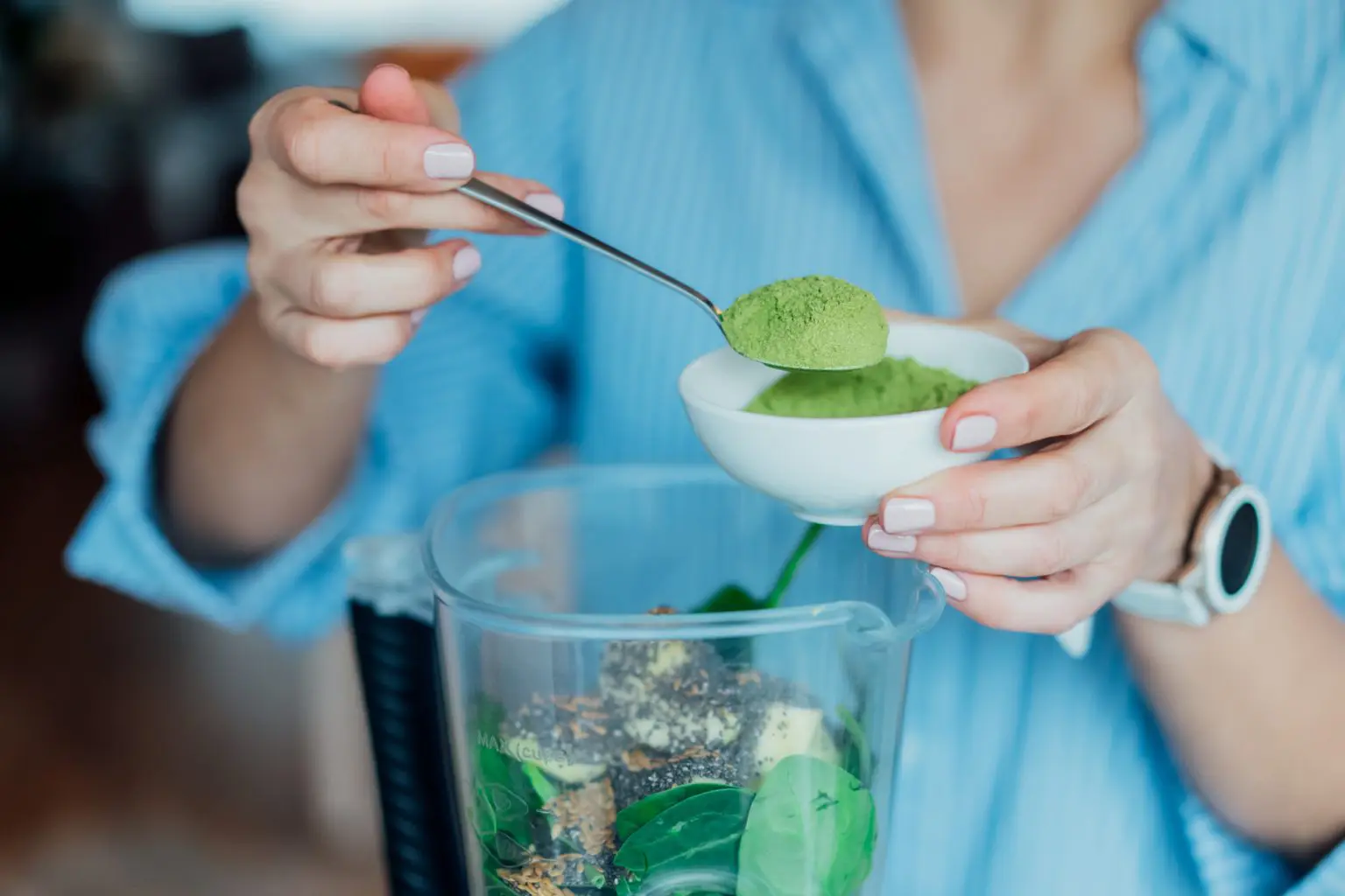 A woman putting green powder into a smoothie machine