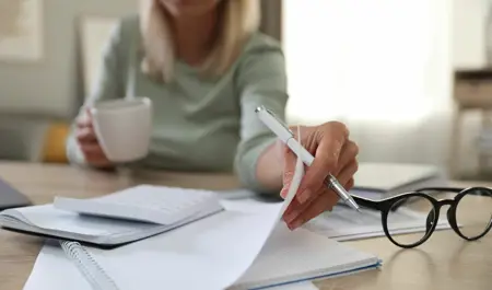 Managing Household Finances for Elderly Care – A woman reviews financial documents while holding a coffee cup, symbolising the responsibility of managing bills, care costs, and financial planning for ageing parents.