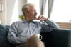 Finding Moments to reflect on your Emotions as a Carent – A silver-haired man sits on a plush sofa, holding a coffee cup while staring thoughtfully into the distance. A representation of taking time for oneself amidst the responsibilities of supporting an ageing parent.