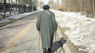 Woman walking with 2 sticks in the cold. Used to represent solo walking by your elderly parent.