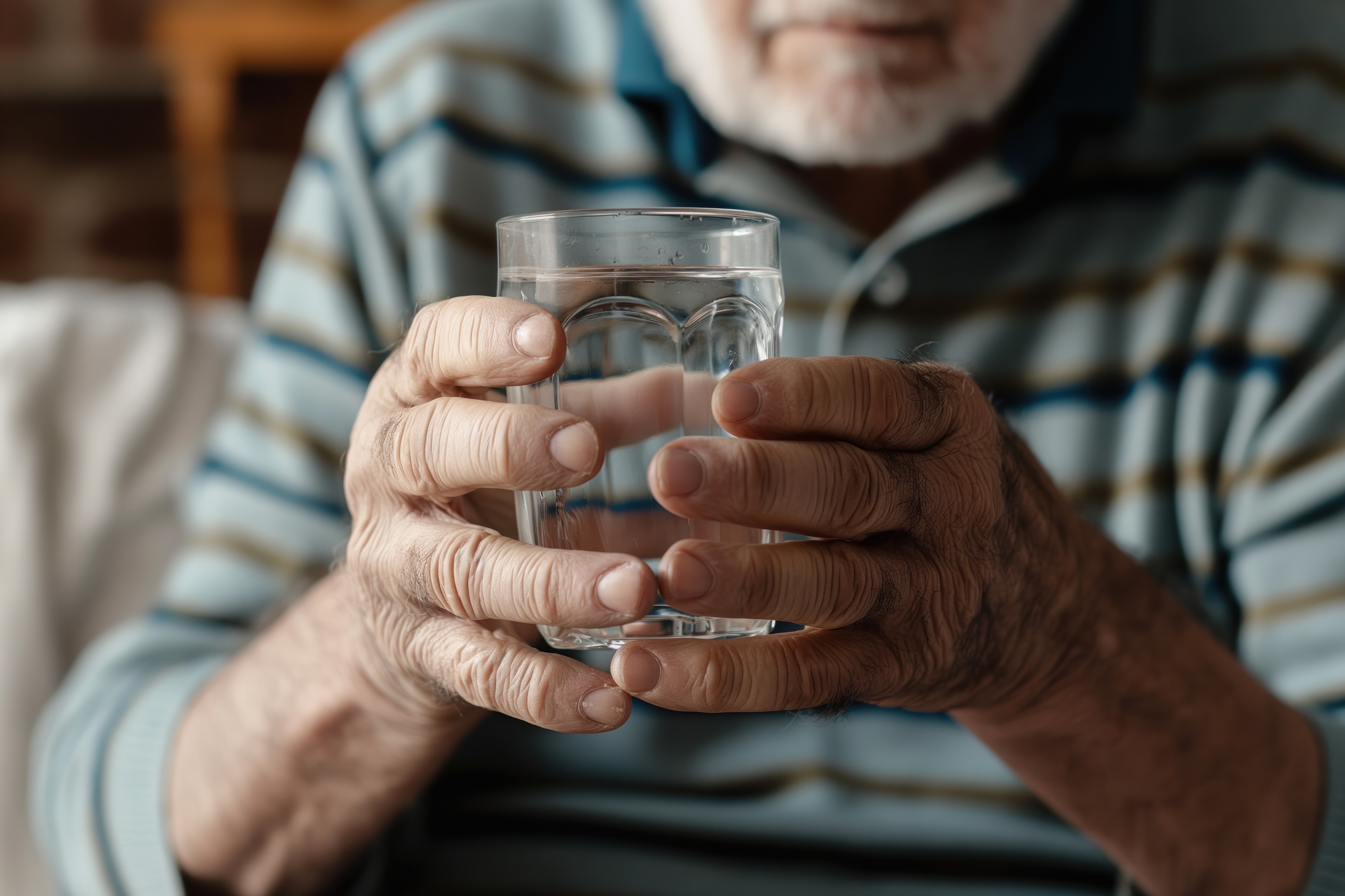 Older adult holding a glass with both hands – highlighting the importance of non-spill cups for elderly parents with limited grip strength, arthritis, or hand tremors to reduce spills and support safe hydration.